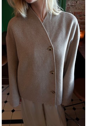 Beige indpakket sweater lavet af blødt stof, med v-hals, lange ærmer og fire runde knapper foran. Glat tekstur.