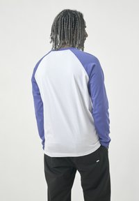 Langarm-T-Shirt mit einem weißen Körper und lilafarbenen Raglanärmeln, aus weichem Stoff mit glatter Textur und lockerer Passform.