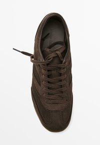Brown suede sneaker with lace-up design, featuring stitched accents and a rounded toe. Smooth inner lining and flat laces.