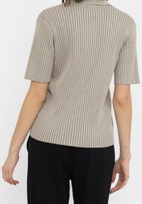 Beige geribbelde gebreide top met korte mouwen, voorzien van een kraag en een getailleerde snit. Textuurstof met een subtiele glans.