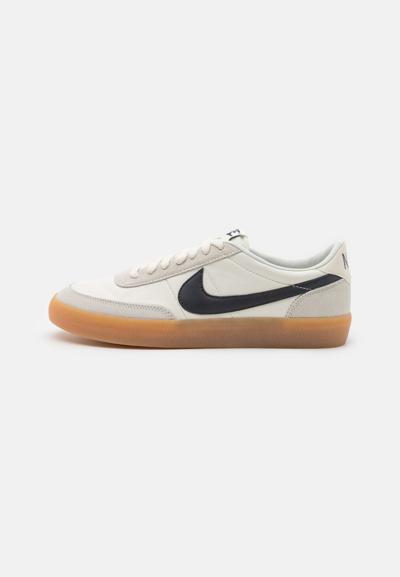 Bílé kožené tenisky s šedými semišovými akcenty, černým logem Nike a gumovou podešví. Mají kulaté tkaničky a nízký profil.