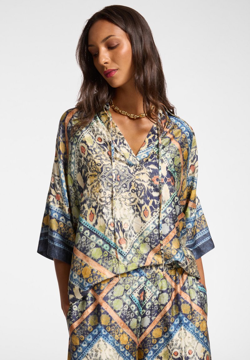 Silkki tunika, jossa on V-pääntie, monivärinen geometrinen ja eläinkuosinen suunnittelu, lyhyet hihat ja rento istuvuus.
