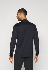 Langärmliges schwarzes Sportshirt mit Stehkragen, glatter Textur und tailliertem Design, mit seitlichen Akzenten und einem klaren Rückansicht.