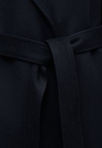 Σκούρο μπλε μάλλινο παλτό με υφασμάτινη ζώνη δεμένη με απλό κόμπο στη μέση.