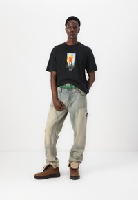 Tricou oversized negru cu un grafic floral, blugi dragoniți, de culoare bleu deschis, și cizme maro cu șireturi, cu detalii pufoase la glezne.