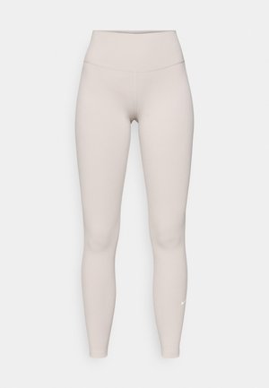 Beige augstās jostas līnijas legingi, izgatavoti no maiga, elastīga auduma, ar gludu tekstūru un mazu baltu logotipu tuvumā potītei.