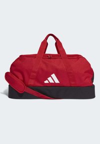 Bolsa de viaje roja con base negra, doble asa y correa de hombro desmontable. Presenta un logo blanco en el lateral y una textura de tela suave.