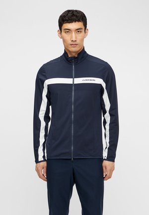 Marineblauwe jas met witte streepdetails, hoge kraag, ritssluiting en een sportief ontwerp. Gemaakt van lichtgewicht stof voor comfort.