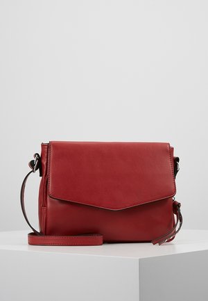 Rød læder crossover taske med klaplukning og justerbar rem, præsenteret på en hvid overflade mod en ensfarvet baggrund.