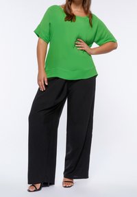Grön kortärmad blus med rund halsringning, matchad med svarta vida byxor. Slät tyg, lös passform och platta sandaler.