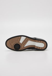 Juodas sportinių batų padas su tekstūruota sukibimo struktūra, su smėlio ir baltu vidiniu padu su prekių ženklu bei apvaliu logotipo akcentu.