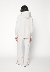 Bílá mikina s kapucí a volnějším střihem, doplněná o široké kalhoty se rozparky na bocích u lemu, vyrobené z měkké látky.