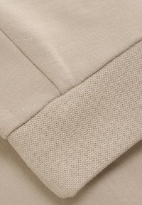 Tissu en coton beige avec une texture lisse et douce et un détail de poignet en maille élastique à côtes. Couture visible le long des bords.