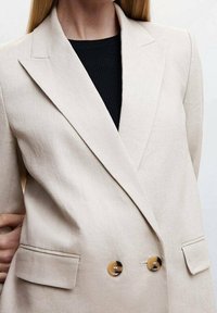 Beige lněný blazer s klopovým límcem, dvouřadým designem, dvěma předními kapsami a knoflíky ve zlatém odstínu. Texturovaný povrch látky.