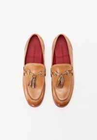 Braune Lederloafers mit glatter Oberfläche, ausgestattet mit einer dekorativen metallischen Quaste und einer roten Innensohle. Runde Zehenpartie und Slipper-Design.