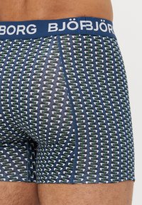 Herren-Boxershorts in einem dunkelblauen, grünen und weißen geometrischen Muster. Mit einem einfarbigen blauen Bund, auf dem "BJÖRG" in weißen Buchstaben steht.
