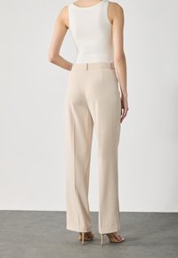 Beige rechtlopende broeken met een soepele textuur en een tailleband. Draagt een witte tanktop met een minimalistisch ontwerp.