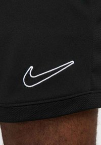 Zwarte sportshorts van textuurstof, met een opvallend wit Nike-logo geborduurd aan de onderlinkerkant.