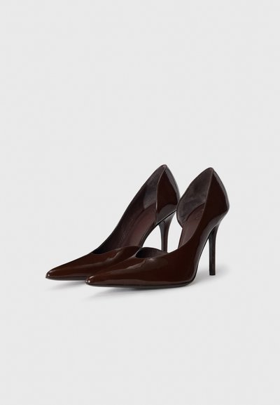 Smeđe lakirane cipele na visoku petu s nazubljenim vrhom i kosim stranicama, s potpeticom šiljastog oblika i minimalističkim dizajnom.