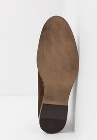 Suola di scarpa in suede marrone con una forma liscia e arrotondata. Superficie texturizzata con scanalature orizzontali e tacco piatto e più scuro.