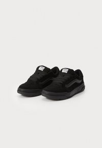 Paire de baskets Vans noires avec lacets et logo sur la languette, présentant une texture en suède et un détail distinctif de bande latérale.
