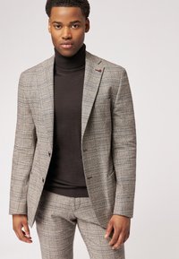 Grau kariertes Anzug mit einem taillierten Blazer und passenden Hosen. Schwarzer Rollkragenpullover darunter. Verfügt über eine maßgeschneiderte Passform und einen dezenten roten Akzent am Revers.