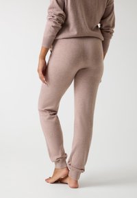 Pantalones de lounge beige claro en un tejido suave, con puños acanalados y un corte ajustado. La parte trasera presenta costuras suaves y una cinturilla cómoda.