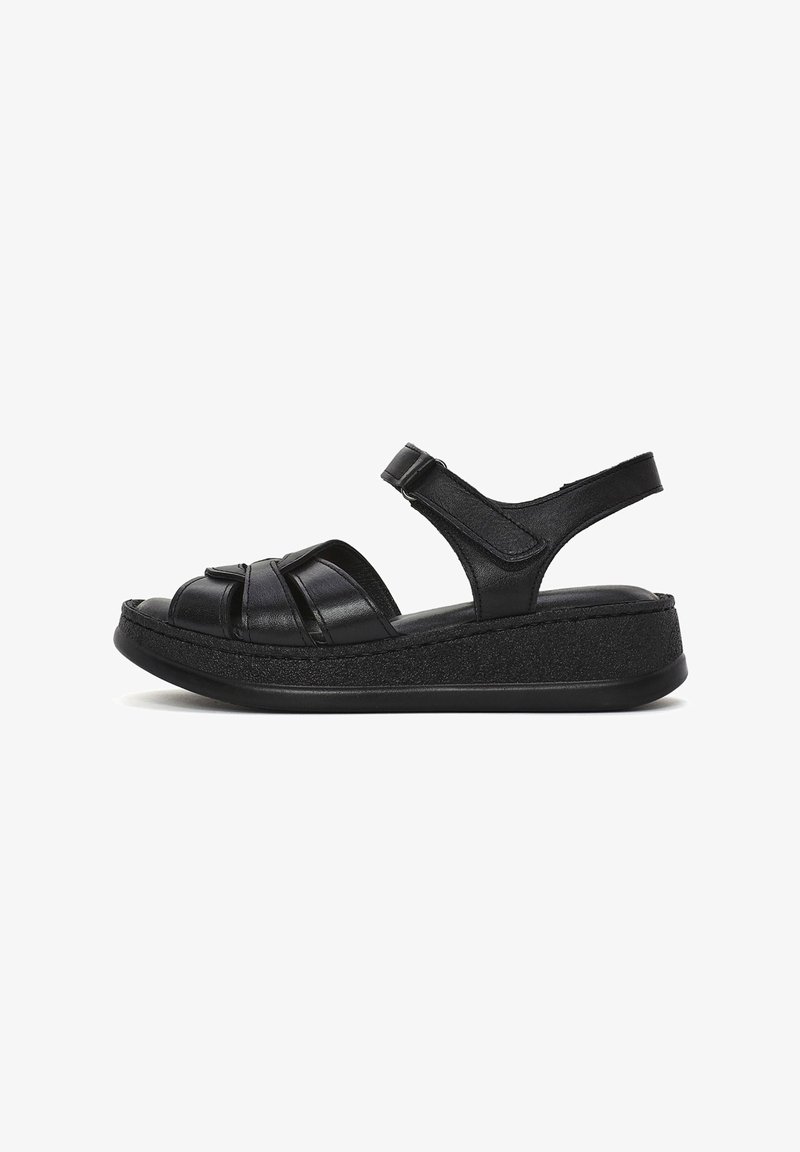 Sandales en cuir noir avec un design à plateforme, présentant des sangles croisées et une sangle arrière pour le soutien. Semelle en caoutchouc noir uni.