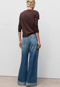 Bruine lange mouwen top gecombineerd met lichtblauwe denim jeans met brede pijpen. De jeans hebben een omgeslagen zoom en achterzakken met donkere stikdetails.