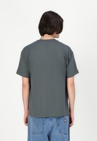 Tricou gri din bumbac cu o croială lejeră, mâneci scurte și decolteu rotund. Prezintă un tiv drept și cusături subtile la decolteu.