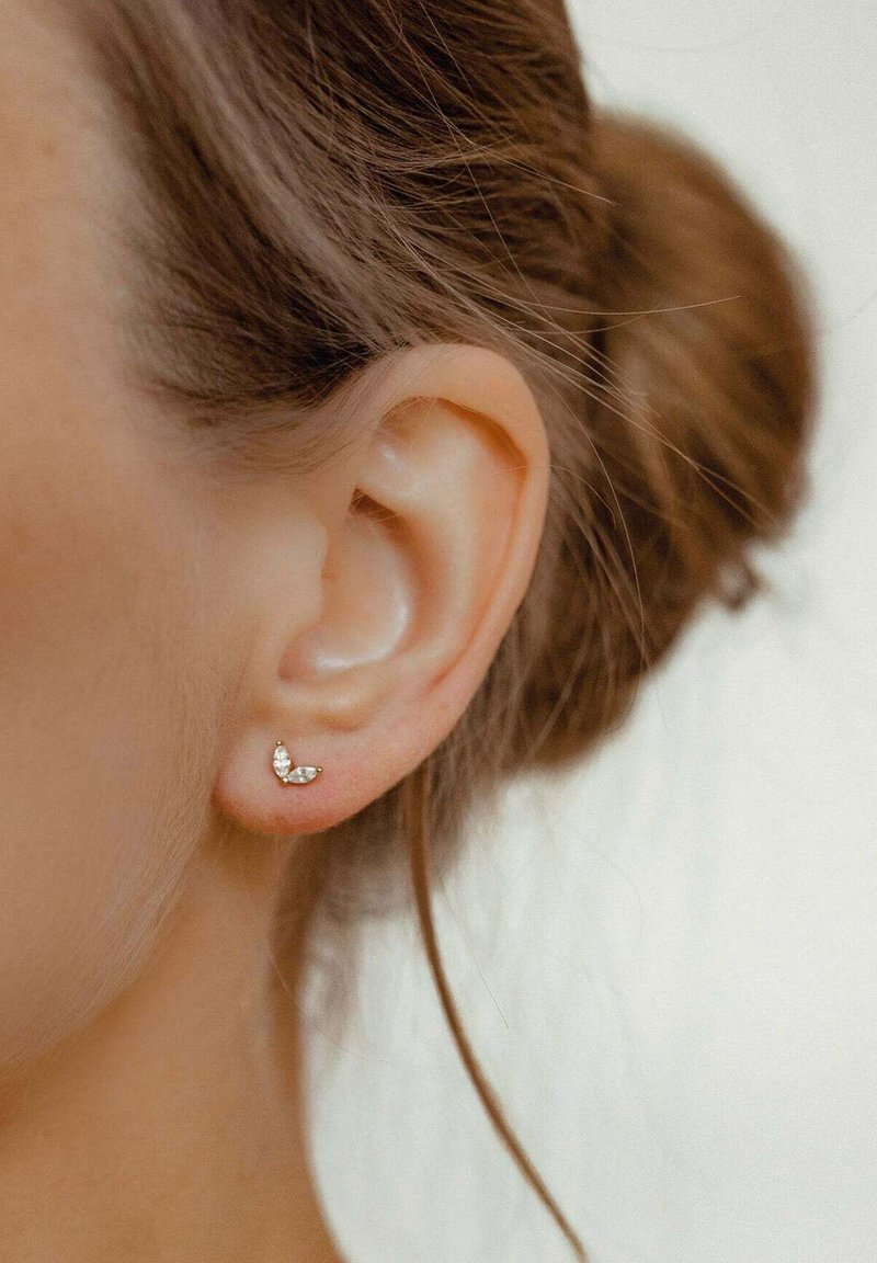 Orecchino argento a forma di farfalla con pietre chiare, indossato su un lobo dell'orecchio forato. I capelli sono raccolti in uno chignon morbido.