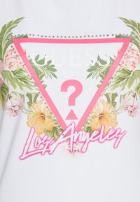 Biała tkanina z różowym trójkątnym logo, kwiatowymi akcentami, dżetami i neonowym różowym napisem "Los Angeles" pod logo.