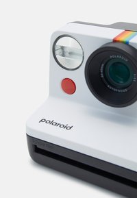 Polaroid camera in white plastic with black base; features green lens, round flash, red button, and rainbow stripe accent.