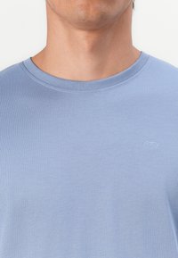 Helles blaues Baumwoll-T-Shirt mit Rundhalsausschnitt und kleinem, geprägtem Logo auf der Brust. Glatte Textur mit lässiger Passform.