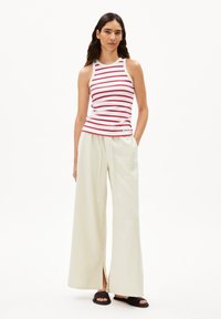 Débardeur rayé rouge et blanc, associé à un pantalon large crème. Fentes sur les côtés du pantalon, porté avec des sandales noires.