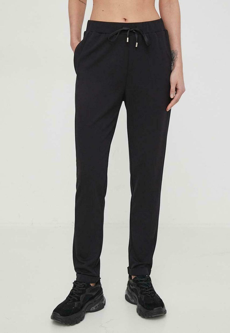 Pantaloni da jogging neri, leggeri, con vita regolabile tramite cordoncino, tasche laterali e vestibilità affusolata. Indossati con scarpe da ginnastica nere.