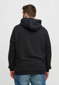 Schwarzer Kapuzenpullover mit weicher Struktur, ausgestattet mit einer Känguru-Tasche und gerippten Bündchen, getragen mit blauen Jeans, von hinten gezeigt.