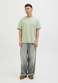 Light green short-sleeve t-shirt with a crew neck, paired with loose-fitting, faded denim jeans and brown slip-on shoes.
