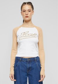 Kraftet langermet skjorte i bomull med hvit kropp og beige raglanermer, med en stor, skriptet logo over brystet. Kombinert med denim jeans.