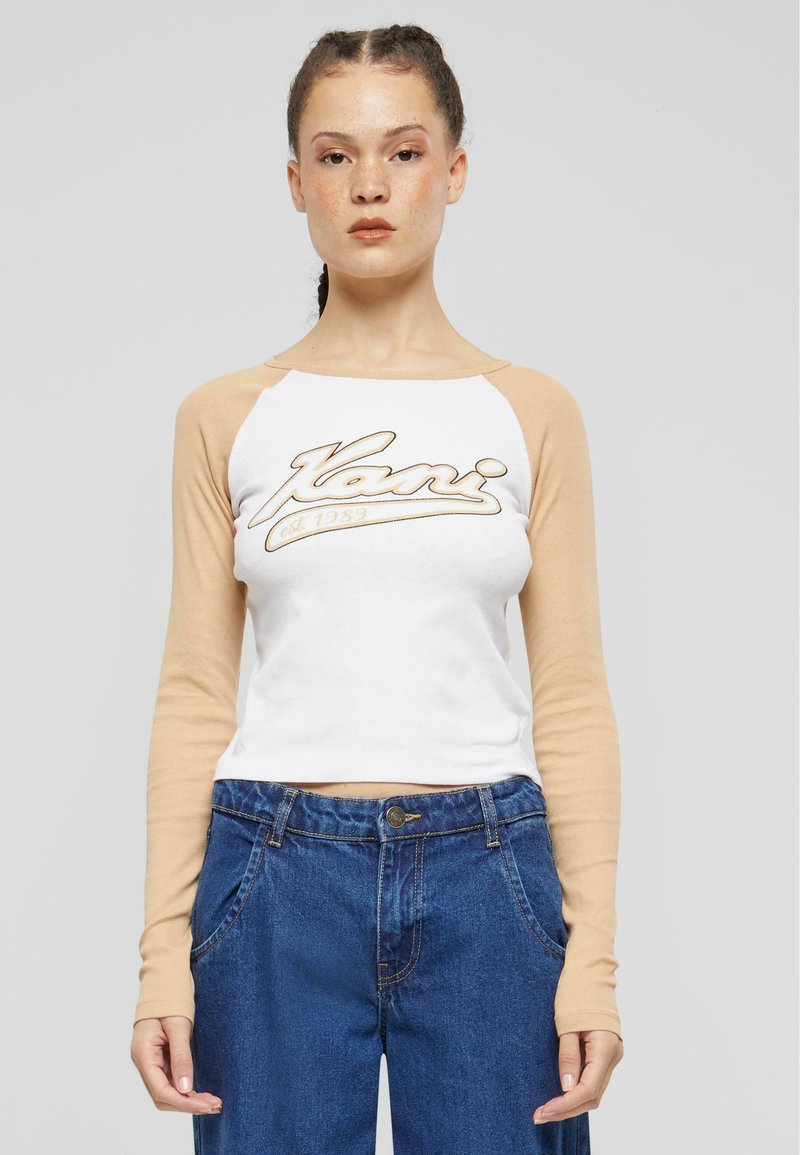 Kraftet langermet skjorte i bomull med hvit kropp og beige raglanermer, med en stor, skriptet logo over brystet. Kombinert med denim jeans.