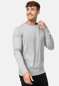 Suéter gris de manga larga hecho de tela suave, con un cuello redondo y puños acanalados, combinado con pantalones negros.
