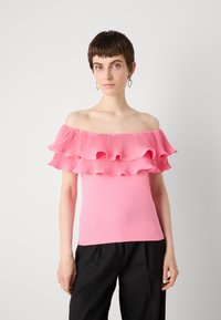 Top de hombros descubiertos en rosa brillante, con dos capas rizadas y pliegues, hecho de una tela suave, combinado con pantalones negros.