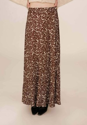 Jupe maxi marron avec un motif abstrait blanc, en tissu léger, taille élastique et une coupe fluide, assortie à des chaussures noires.