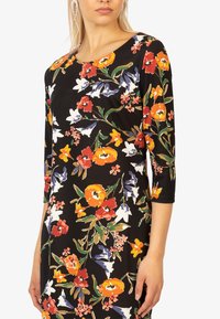 Sorte kjole med et levende blomstermønster med orange, røde og blå blomster. Designet med trekvartærmer og en rund halsudskæring.