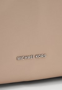 Beige neilona materiāls ar teksturētu virsmu. Sudraba "MICHAEL KORS" logo izcili izceltas modernā fontā.