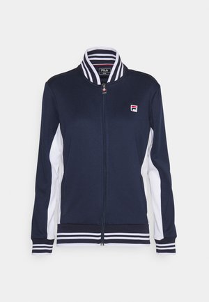 Mørkeblå zip-up jakke med hvide sidepaneler, stribet krave og ribbede manchetter. Har broderet logo på brystet. Blød stoftekstur.