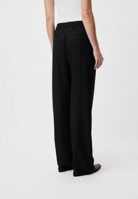 Pantaloni neri a gamba larga con una texture morbida, cintura elastica e una tasca posteriore singola, abbinati a scarpe con tacco basso.