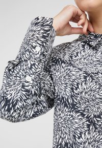 Camicia a maniche lunghe con sfondo navy e motivi floreali bianchi a punte, realizzata in tessuto liscio con bottoni ai polsini.