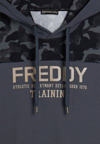 Felpa con cappuccio in grigio scuro con motivo mimetico nero. Presenta scritte bianche "FREDDY" e dettagli di colore bianco. Tessuto liscio con coulisse e punte in metallo.