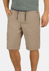 Shorts en coton beige avec une taille à cordon, deux poches latérales et des revers roulés. Présente un petit logo de la marque sur le côté.